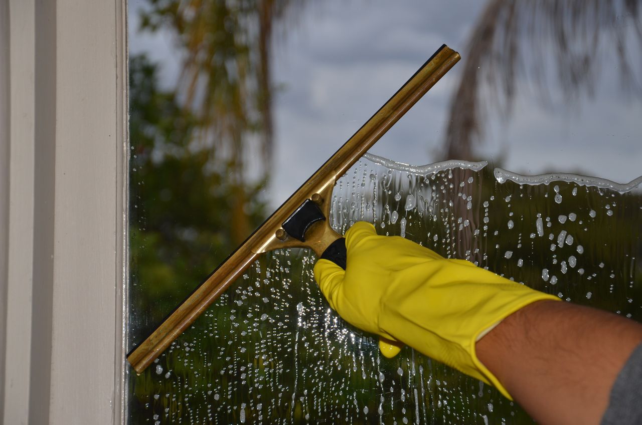 Close-up view of a hand in yellow gloves cleaning an outdoor window with a squeegee.